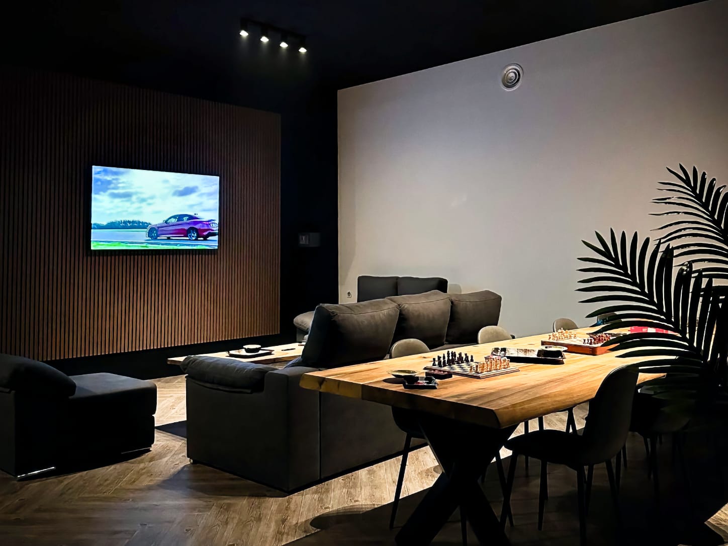 Le salon confortable du club de cannabis Four Twenty &agrave; Valence, avec des canap&eacute;s sombres install&eacute;s face &agrave; un grand &eacute;cran de t&eacute;l&eacute;vision sur un mur en lattes de bois, et des jeux d'&eacute;checs sur une longue table en bois.