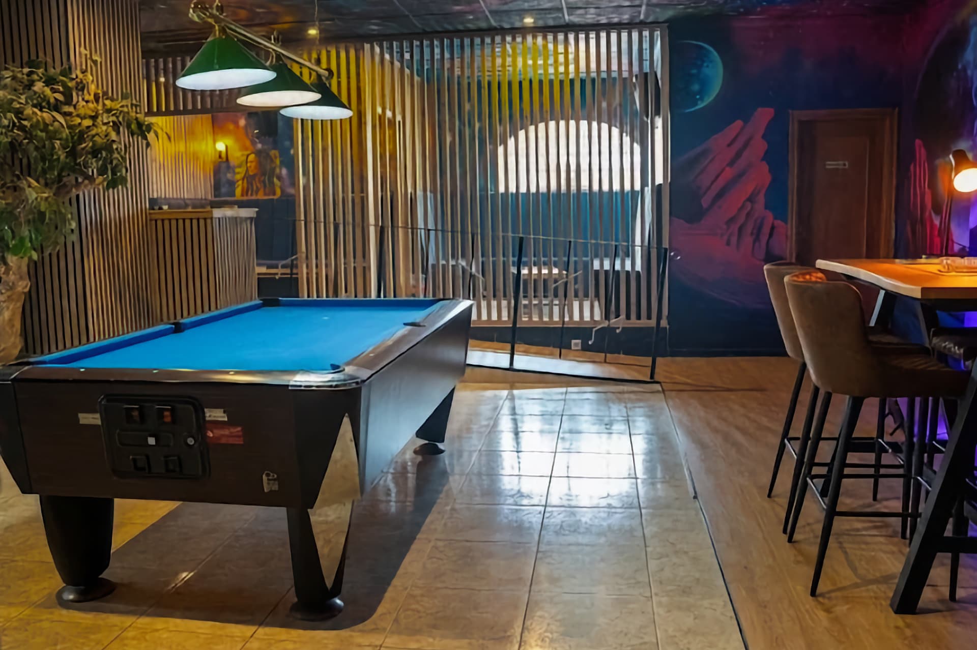 Table de billard dans le club social Sky Alicante avec fresque murale sur le thème de l'espace et cloisons en bois