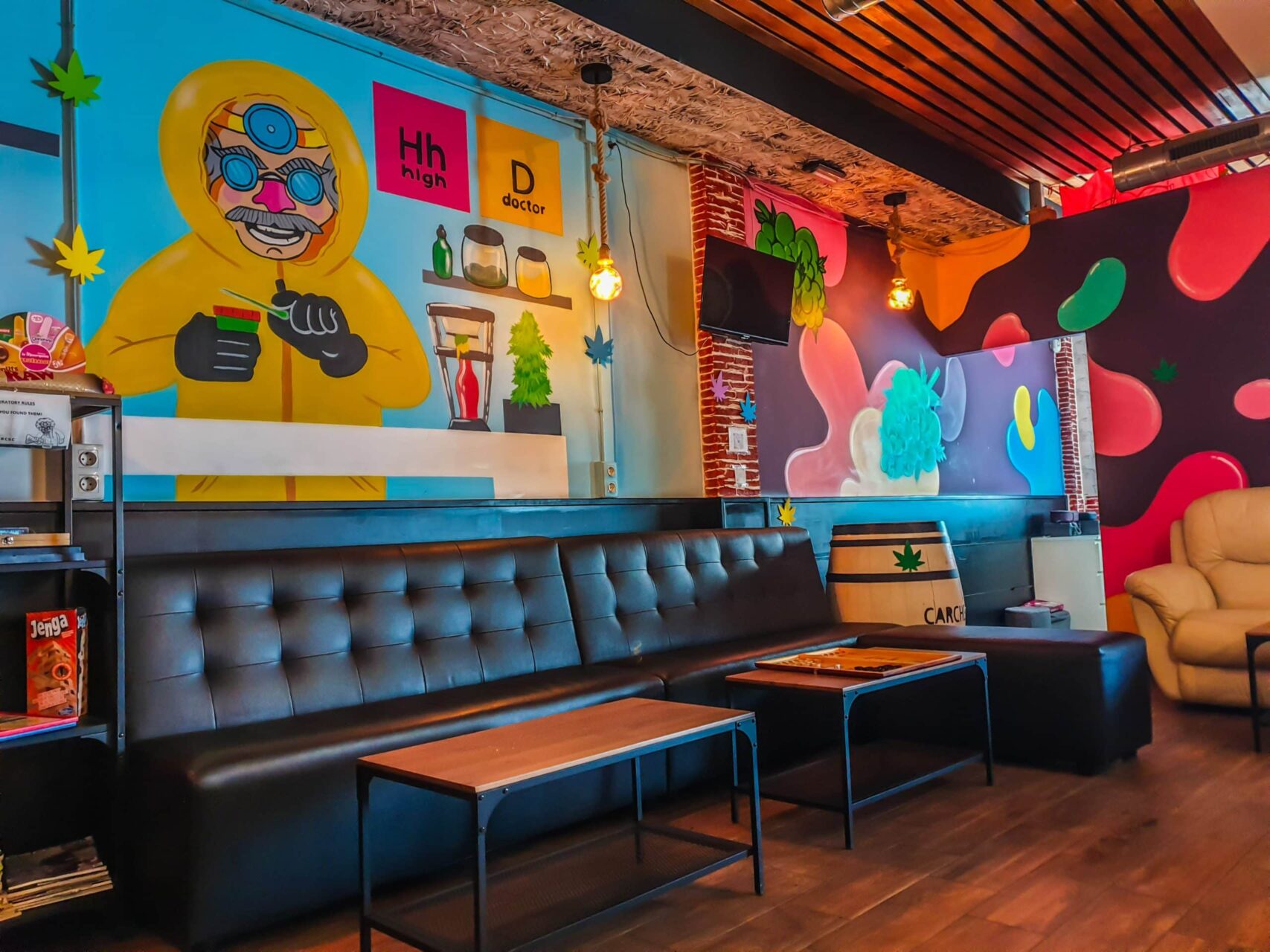 Int&eacute;rieur du social club High Doctor &agrave; Alicante avec murs graffiti color&eacute;s, canap&eacute;s cuir noir et sols en bois.