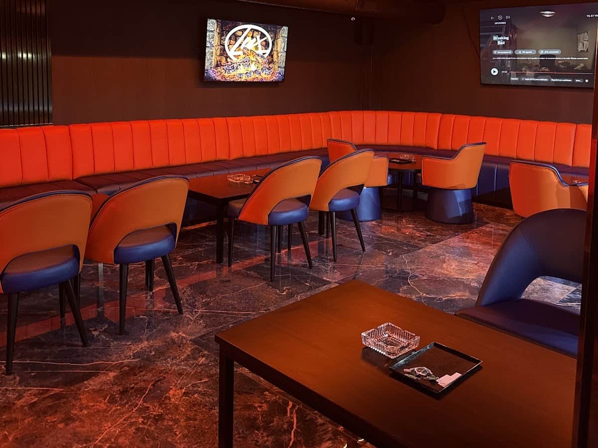 Int&eacute;rieur du Lux Lounge social club &agrave; Marbella avec canap&eacute;s velours orange, &eacute;cran TV et sol en marbre.