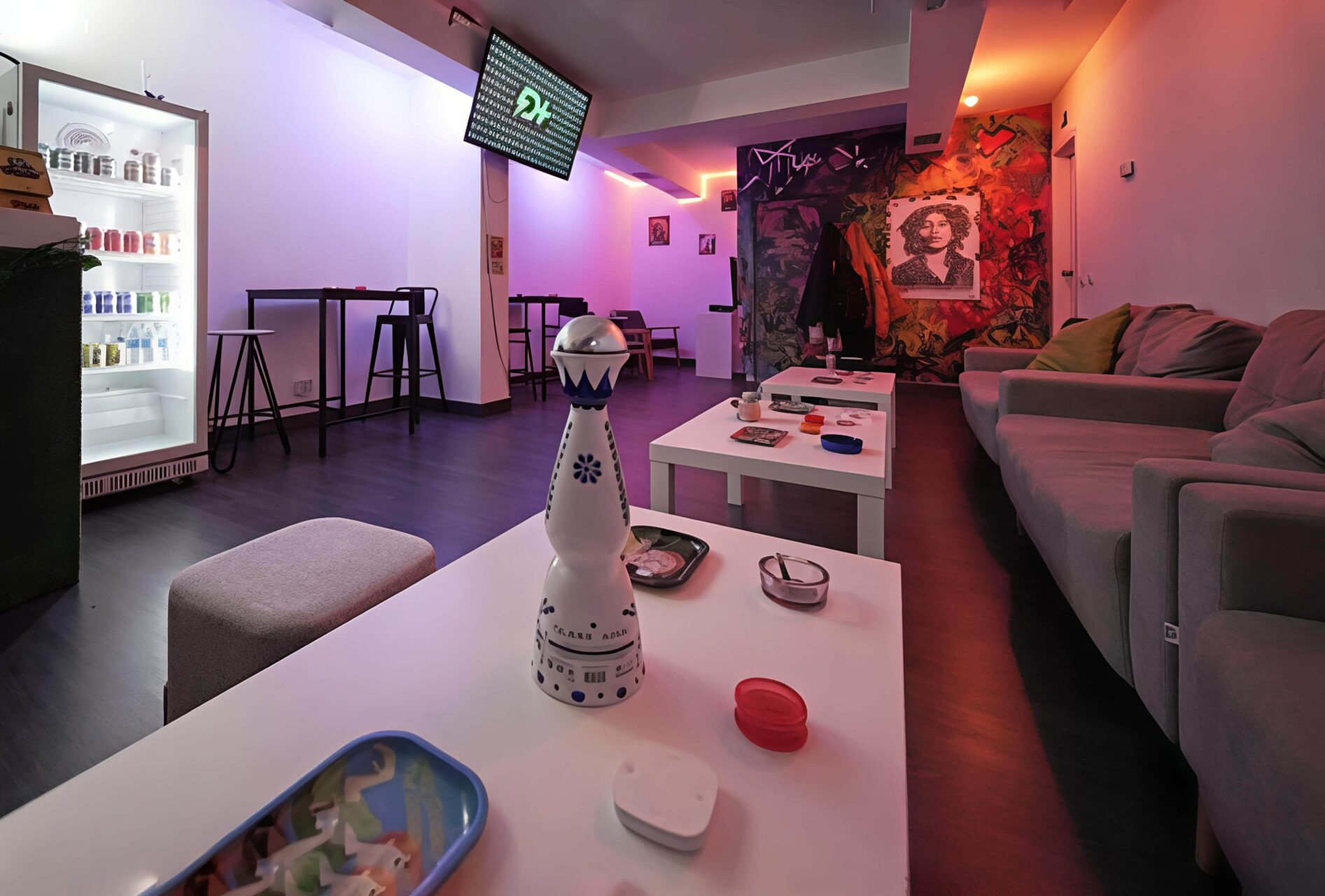 Espace lounge au Valhalla cannabis club &agrave; Madrid avec &eacute;clairage n&eacute;on bleu et orange, tables basses et mur de graffitis.