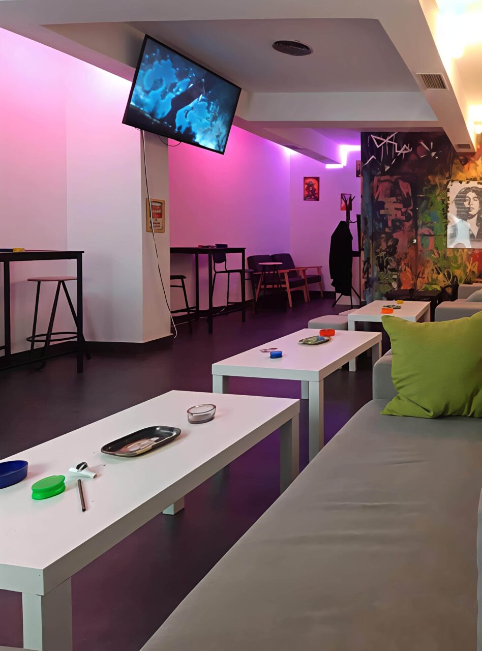 Int&eacute;rieur de lounge moderne avec &eacute;clairage n&eacute;on violet au Valhalla cannabis club &agrave; Madrid, avec tables basses, canap&eacute;s et si&egrave;ges de bar.